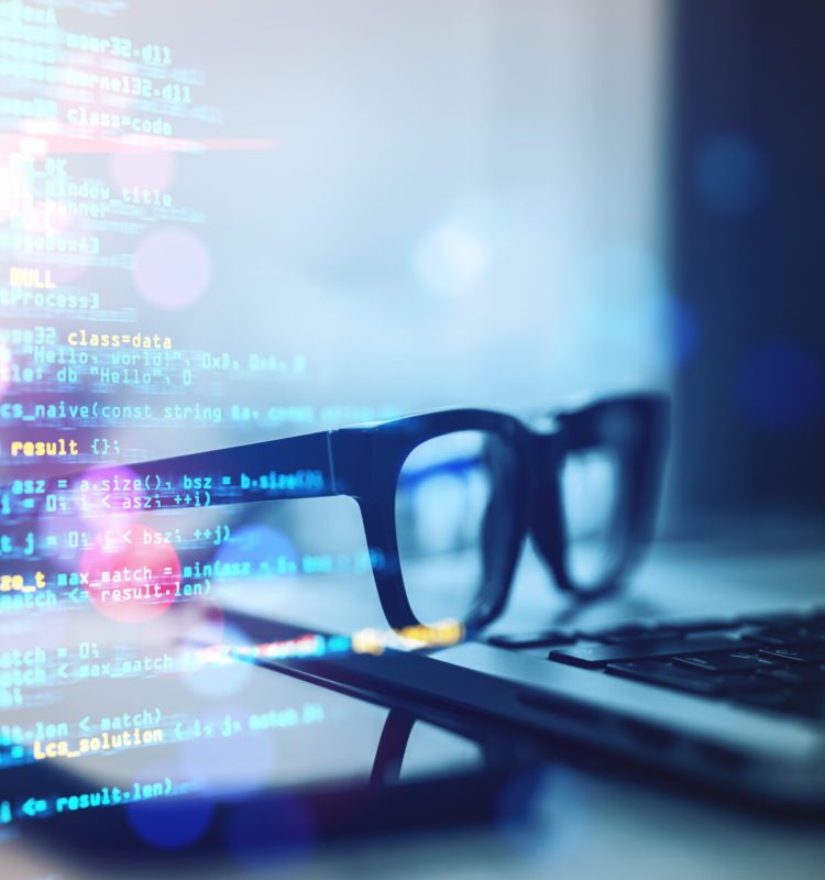 Glasses, laptop, and smartphone on a desk with colorful programming code overlay, abstract blurred background, concept of technology and coding